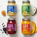 Four jars of Sea Moss Gel with different flavors on a white background, surrounded by natural ingredients.