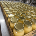 Cardboard box filled with jars of yellow substance and gold lids on a metal surface.