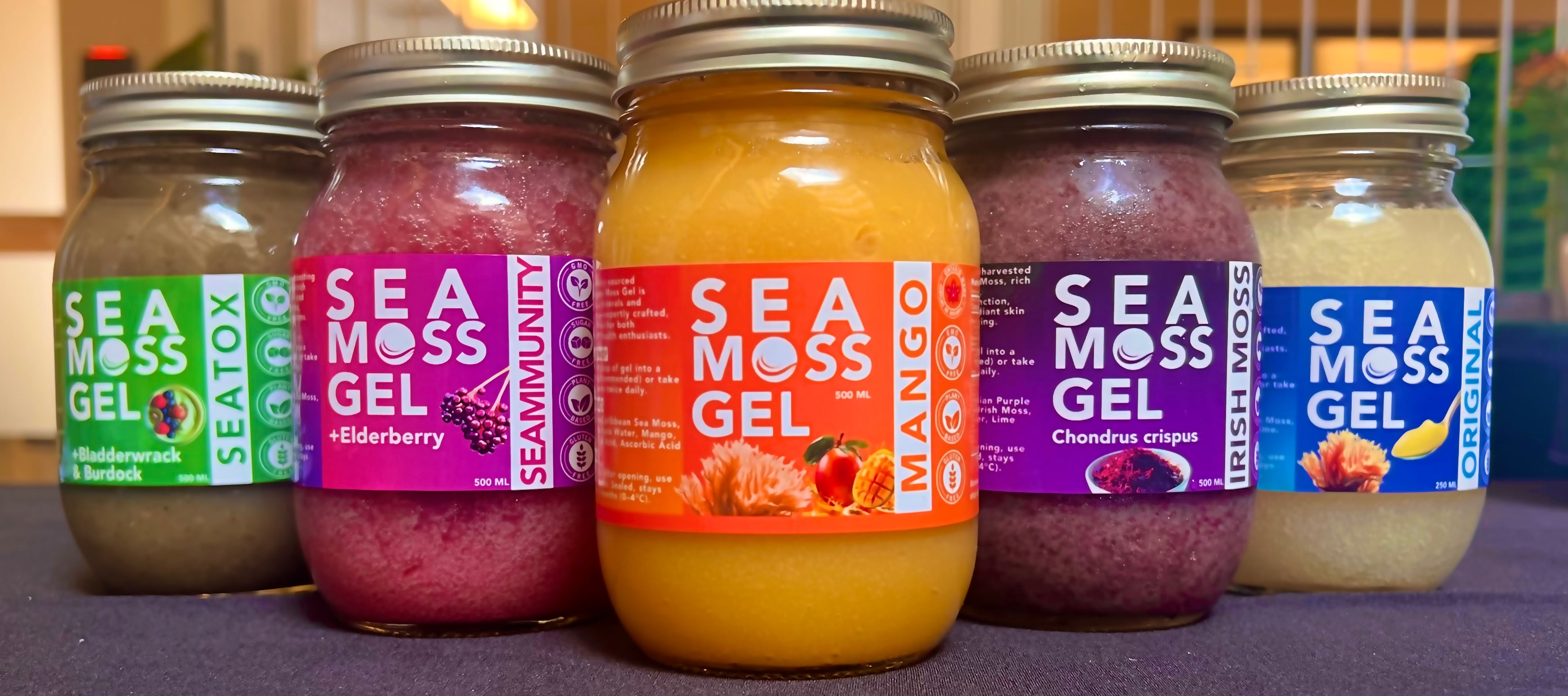 Five jars of Sea Moss Gel with colorful labels on a purple surface.