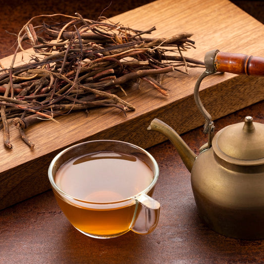 Sarsaparilla root tea in a glass cup next to dried sarsaparilla roots and a teapot, perfect to buy sarsaparilla root tea