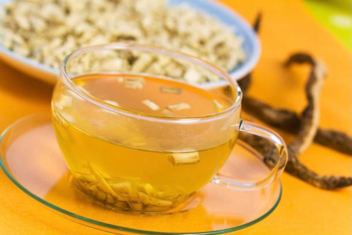 A clear glass cup of tea with marshmallow root for tea, surrounded by dried root pieces