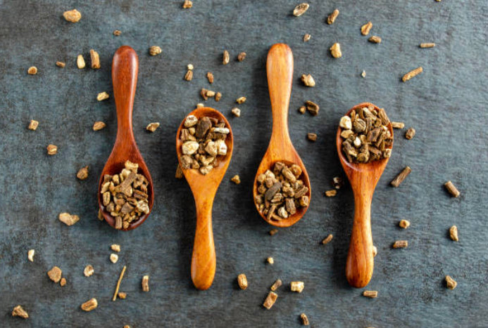 Organic dandelion root pieces in wooden spoons on a rustic surface