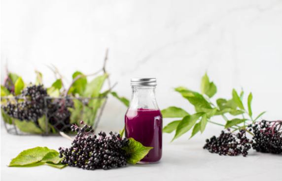 Bottle of elderberry syrup surrounded by fresh whole elderberries for sale and green leaves