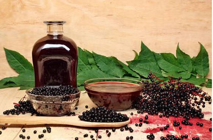 Whole elderberries for sale with a jar of syrup and leaves on a wooden surface